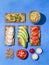 Healthy sandwiches with hummus on rye crackers, with slices of fresh vegetables. Top view on a blue background, hard light