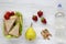Healthy school lunch box with fresh organic vegetables sandwiches, walnuts, bottle of water and fruits on white wooden background,