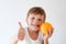 Healthy small smiling kid holding orange fruit and thumb up on white background