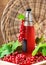 Healthy summer non alcoholic drink of red currant syrup in a glass bottle on a wooden tray with many fresh berries.