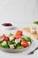 Healthy vegan diet salad of tofu, herbs and tomatoes on white table. two-pronged fork, block of cheese on cutting bamboo board,