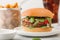 Healthy vegetarian meat free burger on round ceramic plate with vegetables on light table background with potato wedges and glass