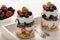 Healthy yogurt dessert with muesli, strawberries, blackberries and blueberries on white wooden table.