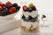 Healthy yogurt dessert with muesli, strawberries, blackberries and blueberries on white wooden table.