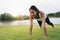 Healthy young Asian runner woman warm up her body by push up before exercise and yoga near lake at park under warm light morning.