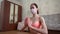 Healthy young gorgeous Caucasian fit girl wear pink face medical mask, sportswear, sit on yoga mat, make Namaste pose at home