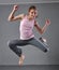 Healthy young muscular teenage girl skipping and dancing in studio. Child exercising with jumping on grey background.