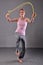 Healthy young muscular teenage girl skipping rope in studio. Child exercising with jumping on grey background.