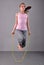 Healthy young muscular teenage girl skipping rope in studio. Child exercising with jumping on grey background.