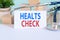 Healts check - text on card on wooden table with stethoscope, medical pills and wooden blocks