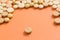 Heap of assorted beige capsules on orange table. One pill is apart, isolated.