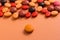 Heap of assorted brown, orange and red capsules on orange table.