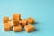 Heap of caramel vanilla fudge on a turquoise background. Fresh tasty candies made of milk and sugar. Square pieces of delicious