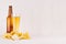 Heap different crispy golden snacks and beer in glass, brown bottle on soft white wood background, with copy space.