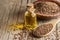 Heap of Flax seeds or linseeds in spoon and bowl with glass of linseed oil on wooden backdrop