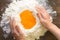 Heap flour with yolks in middle to making a dough with woman hands on wooden background