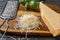 Heap of grated parmesan cheese closeup. Tasty grana padano cheese whole and grated and stainless steel grater on a wooden cutting