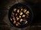 Heap of grilled edible chestnuts in cast iron skillet over dark wooden surface with textile napkin