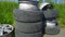 Heap of old used car tires and aluminum rims on a ground against green grass background. Concept of problem of recycling tyre and