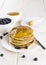 Heap of pancakes watered with honey on a white plate with bilberry on a white wooden table