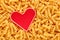 Heap of raw rotini or fusulli pasta with a red heart shape with copy space