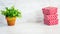 A heap of red dotted gift boxes and a green flower in a rustic ceramic pot. White wooden background, copy space.