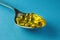 Heap of round fish oil capsules in metallic spoon on blue background