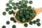 Heap of Spirulina tablets algae nutritional supplement in wooden spoon on white background close up top view