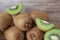 Heap of whole and cut fresh kiwis near wooden wall, closeup