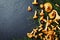 Heap of yellow mushrooms chanterelle cantharellus cibarius with forest plants on dark kitchen table top view. Copy space for tex