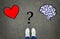 Heart or brain? Legs in white sneakers in front of heart and brain symbols with a question mark between them on the gray asphalt