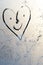 Heart with a drawn face with voices and smile on frosty glass in winter with a finger, heart emoticon drawing by February 14 on