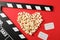 Heart laid out from popcorn, clapperboard and tickets on red background