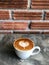 Heart love piccolo latte art in white cup on cement floor and orange brick background
