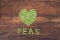 Heart made of fresh locally grown green peas on wooden background