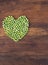 Heart made of fresh locally grown green peas on wooden background