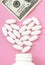 Heart made of pills and money over the neck of a bottle. Expensive medicine and venal love on pink background