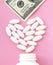 Heart made of pills and money over the neck of a bottle. Expensive medicine and venal love on pink background