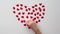 Heart made of shiny red small decorative hearts on a white background with child hand