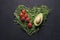 Heart made of young pea shoots, avocado and cherry tomatoes on black background; Top view, flat lay