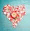 Heart made â€‹â€‹out of pink pale rose petals on blue turquoise background, top view.