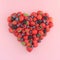 Heart shape of assorted berries on pastel pink background.