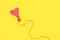 A heart shape deflated pink balloon tied with a sisal yarn on a yellow background