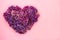 Heart shape made of purple lilac flowers on pastel pink background. Love symbol. Copy space. Top view