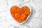 Heart shaped bowl with apricots on marble background, top view.