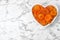 Heart shaped bowl of apricots on marble background, top view with space for text. Dried fruit