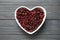 Heart shaped bowl with cranberries on wooden background, top view. Dried fruit