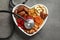 Heart shaped bowl with dried fruits, nuts and stethoscope on grey background