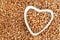 Heart-shaped bowl of roasted buckwheat on groat background