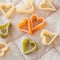 Heart-shaped colored Italian pasta from durum wheat with vegetables on the kitchen textiles, background for Valentine
